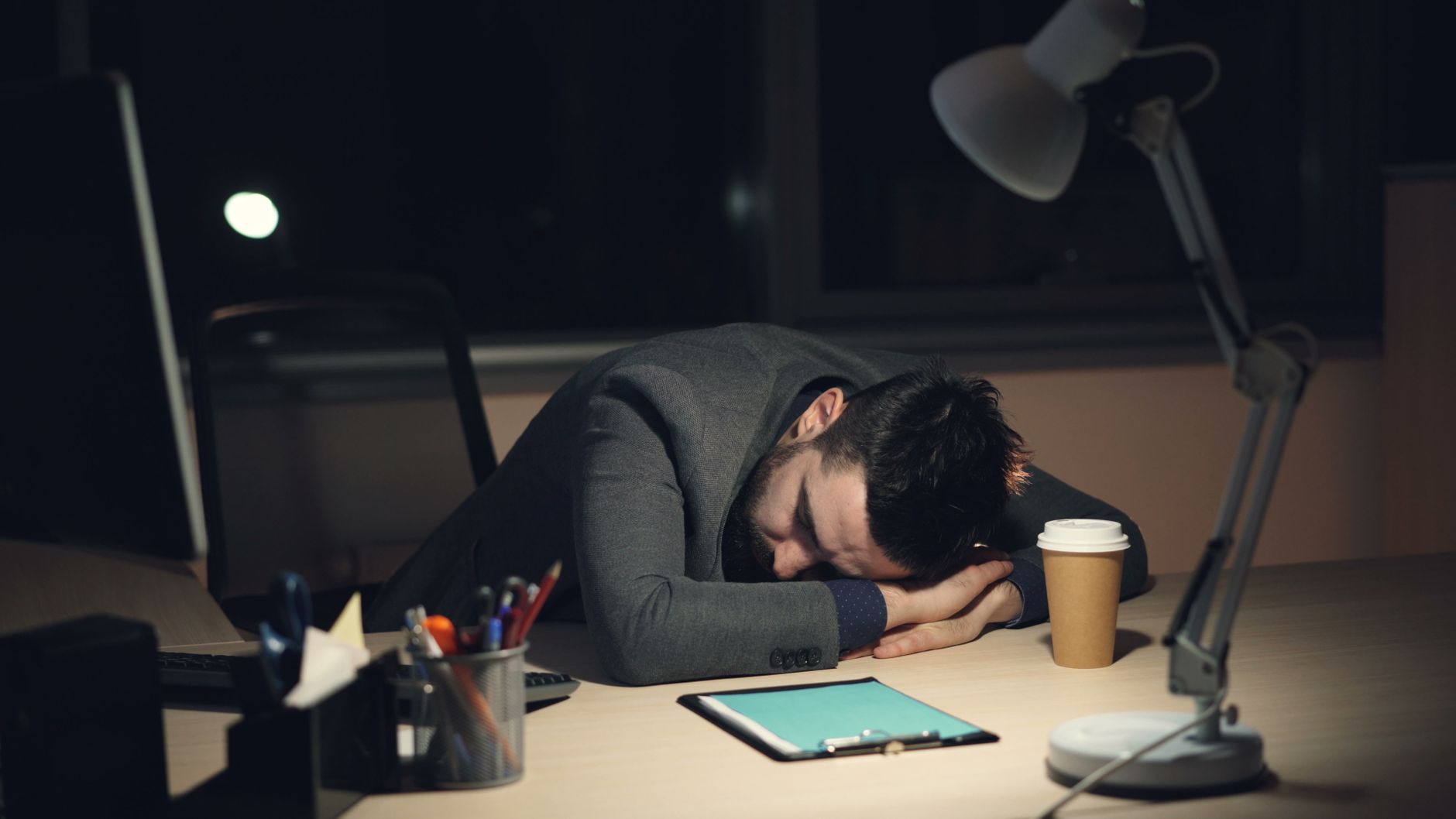 Persona agotada con la cabeza apoyada sobre el escritorio por burnout, junto a una lámpara y una tablet